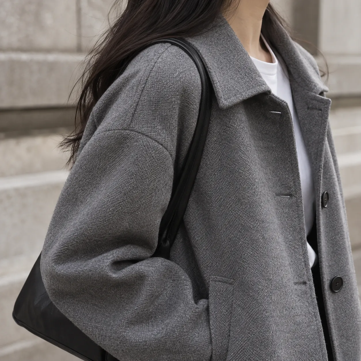 Detail of a grey wool-blend coat with dropped shoulders over a white tee