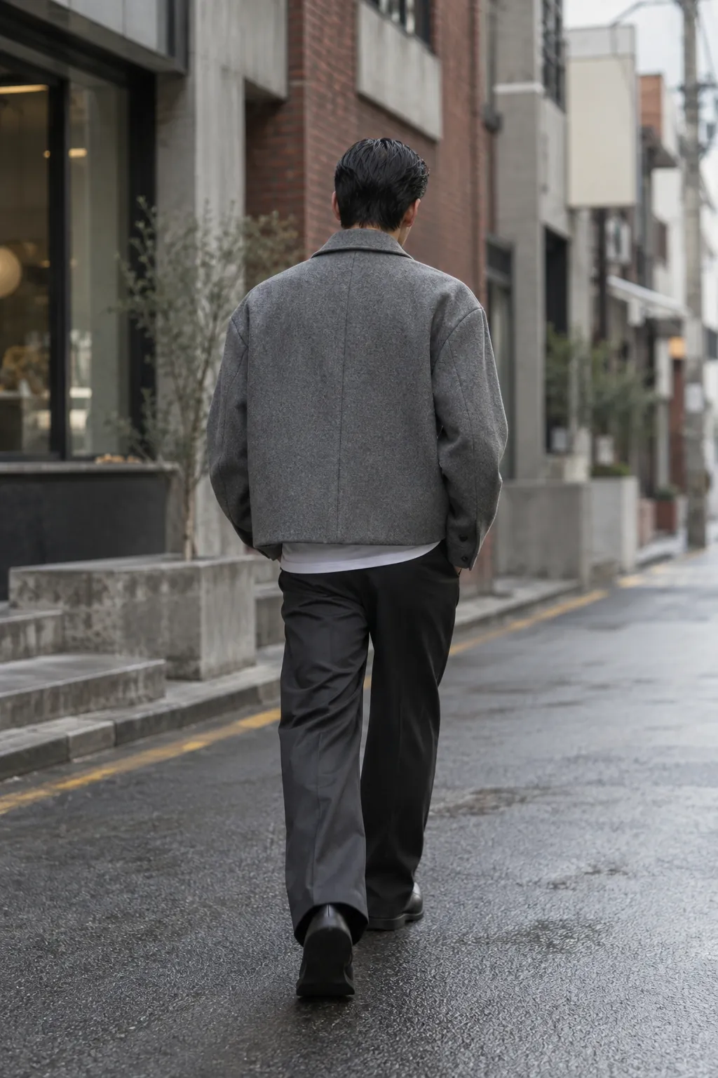 A person in a grey short coat walking down a wet Seoul street, from behind